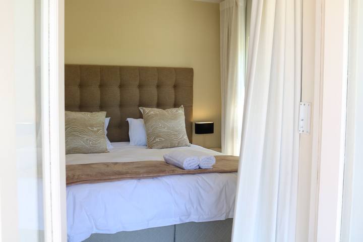 A double bed with a tufted headboard and neatly folded towels, seen through the bedroom doorway