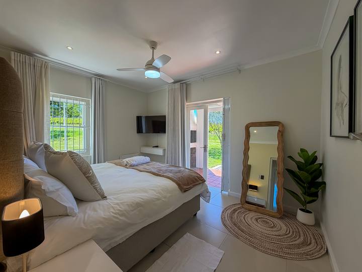 A bedroom with a king bed, a wooden floor mirror and jute rug, and a door out to the garden