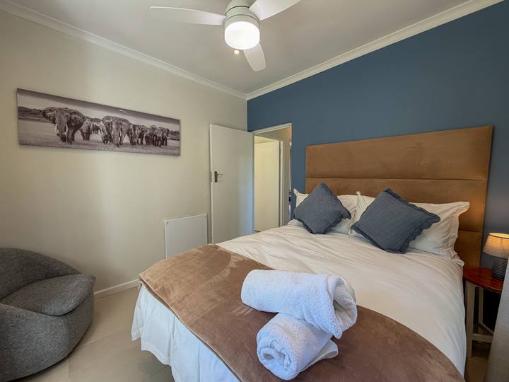 A bed with a tan headboard and blue accent wall, with folded white towels and an elephant print above