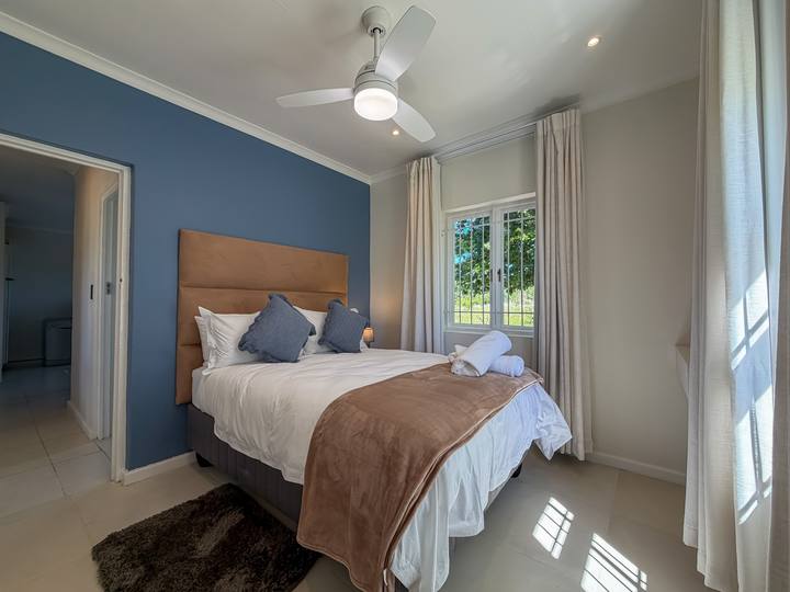 A second bedroom with a blue feature wall, tan headboard and a view through to the next room