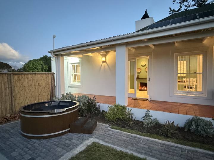 The cottage patio at dusk with the wooden hot tub and a fire glowing through the lit windows