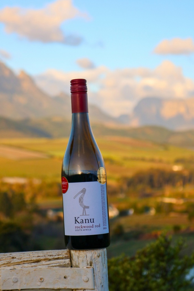 A bottle of Kanu Rockwood Red on a fence post with the Stellenbosch mountains and vineyards glowing at sunset behind