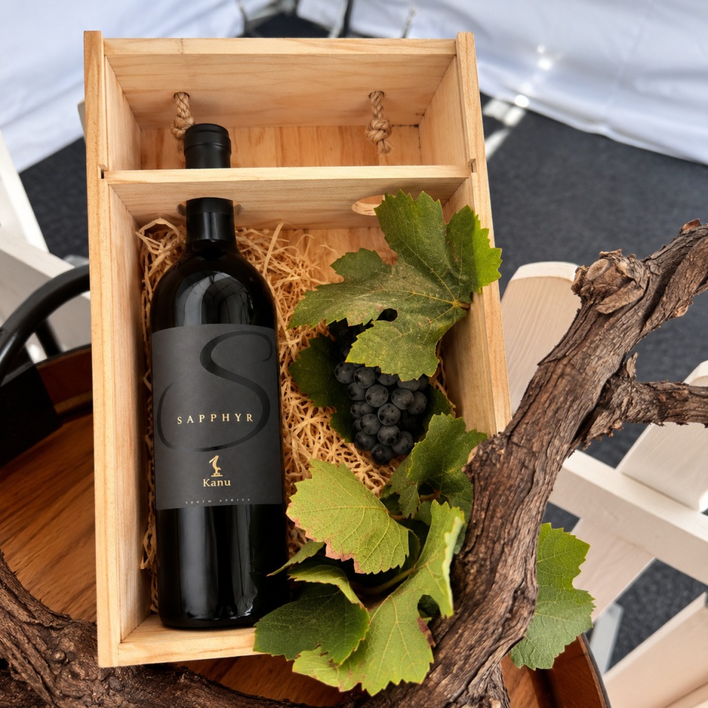 A bottle of Kanu Sapphyr in a wooden gift box with vine leaves, grapes and an old vine stump